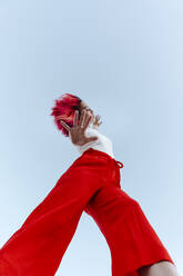 Young woman doing stop gesture while standing against blue sky - TCEF01029