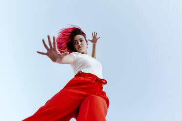 Young woman with dyed red hair doing stop gesture while standing against clear sky - TCEF01030