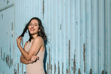 Portrait of happy brunette young woman standing at a run down wall - GRCF00340