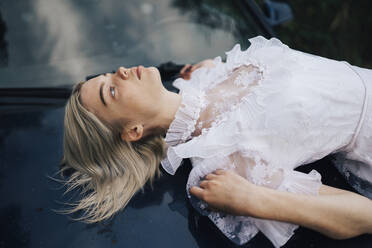 Woman lying on the hood of a car in a white dress - CAVF88610