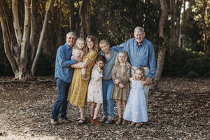 Porträt einer großen lächelnden Großfamilie, die sich draußen im Wald umarmt - CAVF88617