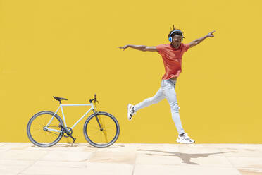 Energetic ethnic guy jumping near bicycle - CAVF88628