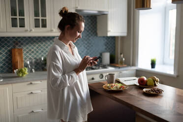 Businesswoman browsing smartphone during breakfast - CAVF88638