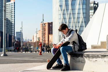 Junger Backpacker-Teenager sitzt im Freien und benutzt ein Smartphone - CAVF88646