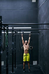 Hemdfreier fitter junger Mann beim Training in einem Käfig in einem Fitnessstudio - CAVF88650