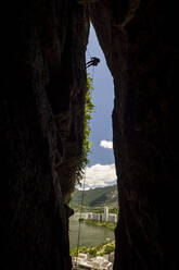 View to silhouette of rock climber man rappelling on mountain crack - CAVF88704