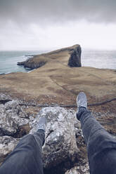 UK, Schottland, Beine eines Mannes auf Felsen am Neist Point sitzend - RSGF00256