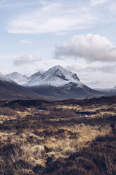 Vereinigtes Königreich, Schottland, Braune Graslandschaft der Isle of Skye im Winter mit schneebedeckten Bergen im Hintergrund - RSGF00274