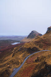 UK, Schottland, Drohnenansicht einer leeren Autobahn, die sich entlang der braunen Berglandschaft der Isle of Skye mit einem kleinen See im Hintergrund erstreckt - RSGF00278