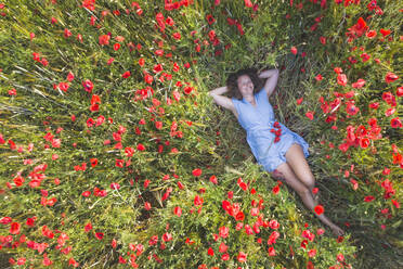 Smiling woman lying with hands behind head on poppy field - ASCF01450