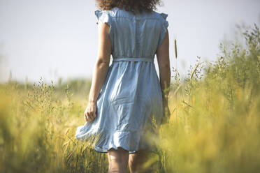 Woman in blue dress walking in agricultural field - ASCF01454