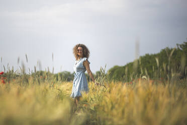 Young beautiful woman smiling while standing in poppy field - ASCF01462