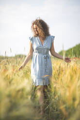 Junge Frau sieht sich die Ernte an, während sie auf einem landwirtschaftlichen Feld spazieren geht - ASCF01463