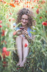 Young woman using mobile phone while sitting in agricultural field - ASCF01481