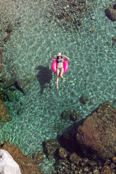 Von oben weiblich in Badebekleidung und Sonnenbrille Schwimmen in transparentem Wasser mit aufblasbarem Schlauch an einem sonnigen Tag am Urlaubsort - ADSF13787