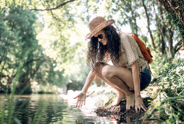 Side view of female tourist sitting on stones near calm river during summer vacation - ADSF13789