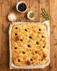 Draufsicht auf traditionelles italienisches Focaccia-Brot mit Oliven, Rosmarin und Salz auf einem Holztisch - ADSF13796