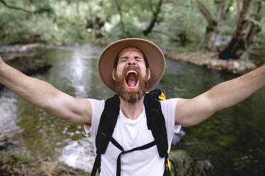 Junger Mann mit Bart Hut auf dem Kopf und gelben Rucksack Wandern entlang eines Sees Route mit Bäumen und schattigen Bereichen ein Selfie nehmen - ADSF13817