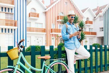 Trendy erwachsenen Mann Surfen Smartphone stehen auf der Promenade mit Vintage-Fahrräder gegen Costa Nova Häuser - ADSF13833