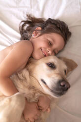 Top view of cheerful child on bed hugging adorable Hovawart at home - ADSF13871