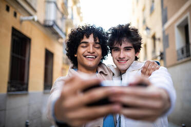 Multiethnisches homosexuelles Paar, das sich auf der Straße umarmt und ein Foto mit dem Handy macht - ADSF13877