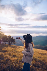 Seitenansicht einer nicht erkennbaren weiblichen Reisenden, die im Herbst auf einem Hügel im Hochland steht und ein Foto mit einer Handykamera während eines herrlichen Sonnenuntergangs macht - ADSF13928