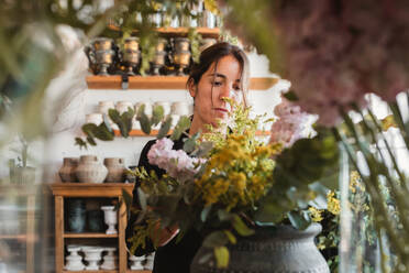 Front view of concentrated female designer arranging decorative blooming bouquets while working on order for event in creative floristry studio - ADSF13931