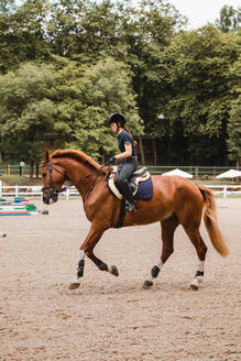 Reiterin in Uniform reitet Fuchs auf Sandplatz während Dressur an bewölktem Tag - ADSF13952