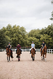 Kompanie weiblicher Jockeys in Uniform in Sätteln reitet auf Kastanienpferden auf einem sandigen Platz - ADSF13953