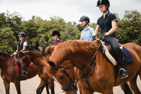 Kompanie weiblicher Jockeys in Uniform in Sätteln reitet auf Kastanienpferden auf einem sandigen Platz - ADSF13954