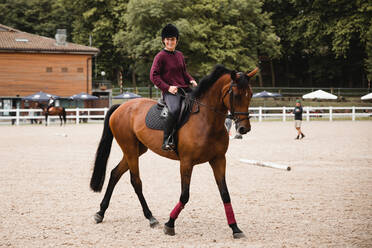 Lächelnde Reiterin in Uniform reitet auf einem Fuchs auf einem Sandplatz beim Dressurreiten und schaut in die Kamera - ADSF13955