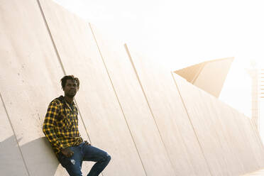 Junger afrikanischer Mann lehnt sich bei Sonnenuntergang an eine moderne Betonstruktur, Lifestyle-Konzept - ADSF13970