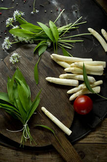 Geschälter Spargel, gebündelter Bärlauch, Tomate und Schneidebrett auf rustikalem Backblech - ASF06670