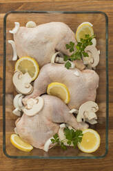 Uncooked chicken with tomatoes lemon and mushrooms in glass oven recipient resting on a wooden table - ADSF13998