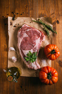 Draufsicht auf rohes Rindfleisch auf Bastelpapier auf einem Tisch mit frischen Tomaten und Olivenöl mit Gewürzen und Knoblauch angeordnet - ADSF14012