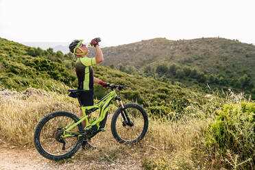 Man in helmet drinking water near bike in mountain - ADSF14067