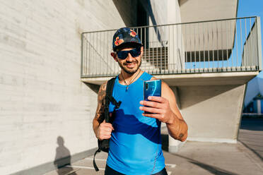 Zufriedener Sportler in Sportkleidung, der auf der Straße steht und ein Selfie mit der Handykamera nach dem Training in der Stadt macht - ADSF14131