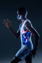 Side view of serious athletic African American sportsman in colorful active wear performing running fast movement in dark studio with red neon illumination - ADSF14148