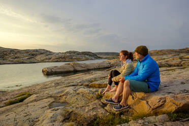 Sweden, Vastra Gotaland County, Grebbestad, Man and teenage girl sitting together on coastal rocks at Tjurpannans Nature Preserve - LBF03199