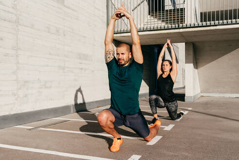 Paar in Sportkleidung übt Yoga in Halbmond-Longe-Pose mit erhobenen Armen und meditiert - ADSF14187