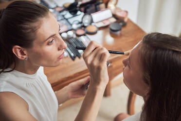 Crop fokussiert Make-up-Künstler Anwendung schwarzer Eyeliner auf junge schöne weibliche Client Augenlider während der Arbeit in zeitgenössischen Studio - ADSF14194