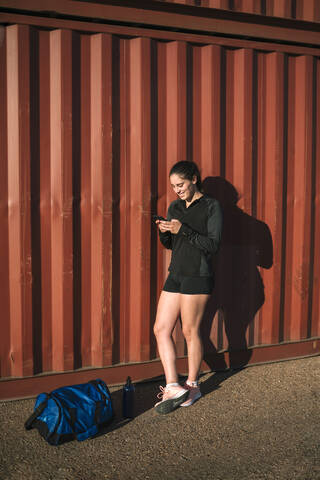 Sportliche Frau benutzt Smartphone im Industriegebiet, lizenzfreies Stockfoto