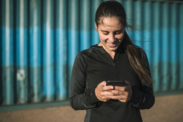 Sportliche Frau benutzt Smartphone im Industriegebiet - GRCF00361