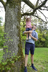Verspielte Tochter mit Vater Unterstützung hängen auf Zweig des Baumes im Wald - ECPF01015