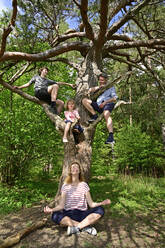 Mann mit spielenden Kindern, während die Mutter unter einem Baum im Wald meditiert - ECPF01029