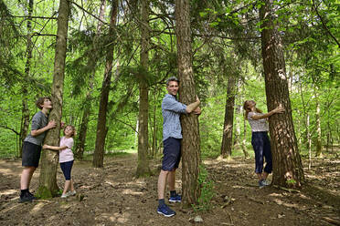 Family embracing tree while standing in forest - ECPF01031