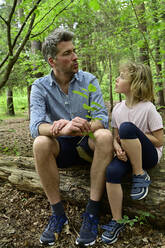 Vater im Gespräch mit seiner Tochter auf einem Baumstamm im Wald sitzend - ECPF01036