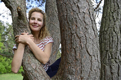 Smiling woman embracing while sitting on tree in forest stock photo