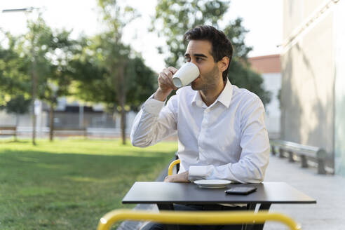 Geschäftsmann, der in einem Straßencafé sitzt und Kaffee trinkt - AFVF07124