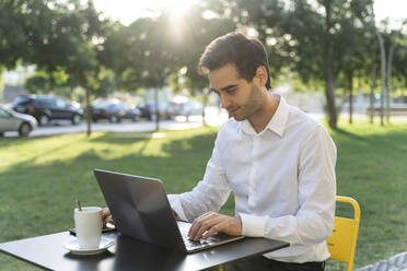 Businessman using laptop on table while sitting at sidewalk cafe - AFVF07127